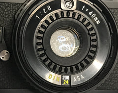 Lens of the Sears 35rf rangefinder with a light shining through it to show the dust inside
